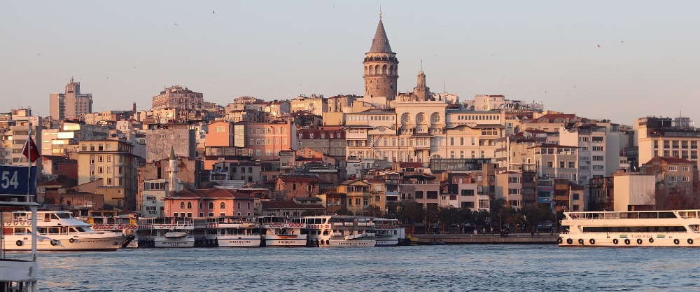 Vista del horizonte de Estambul al atardecer, destacando la icónica Torre de Gálata sobre un denso paisaje urbano de edificios históricos y barcos navegando por las aguas del Cuerno de Oro.
